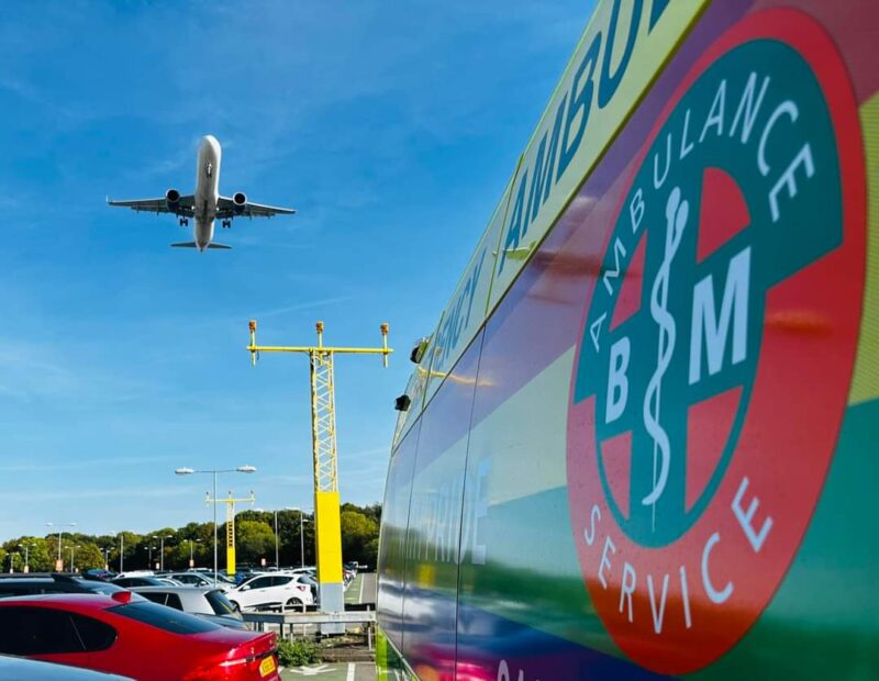 BM Ambulance vehicle positioned for London airport ambulance transfer as aircraft approaches for patient transfer between aircraft and hospital